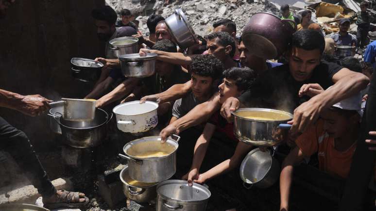 Moradores da Faixa de Gaza se aglomeram para conseguir comida em uma cozinha comunitária em Jabalia, no norte do enclave palestino, nesta segunda-feira, 19 de maio de 2025.